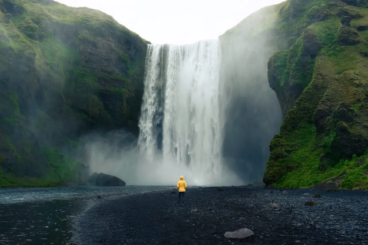 Skogafoss waterfall flowing with a woman standing in summer, Iceland