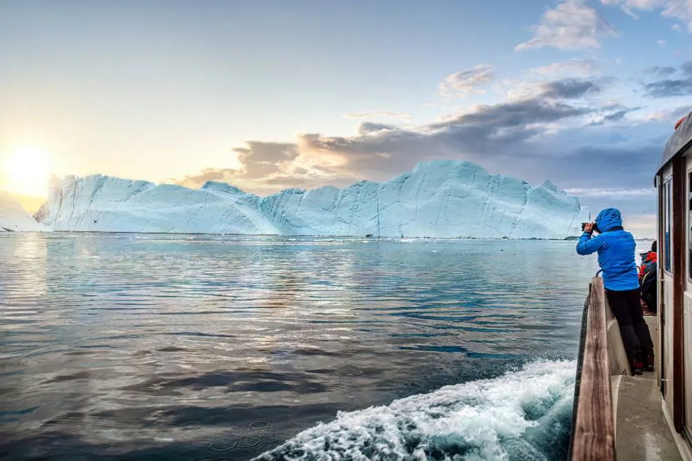 Person on boat taking photograph of iceberg near Ilulissat — Getty Images