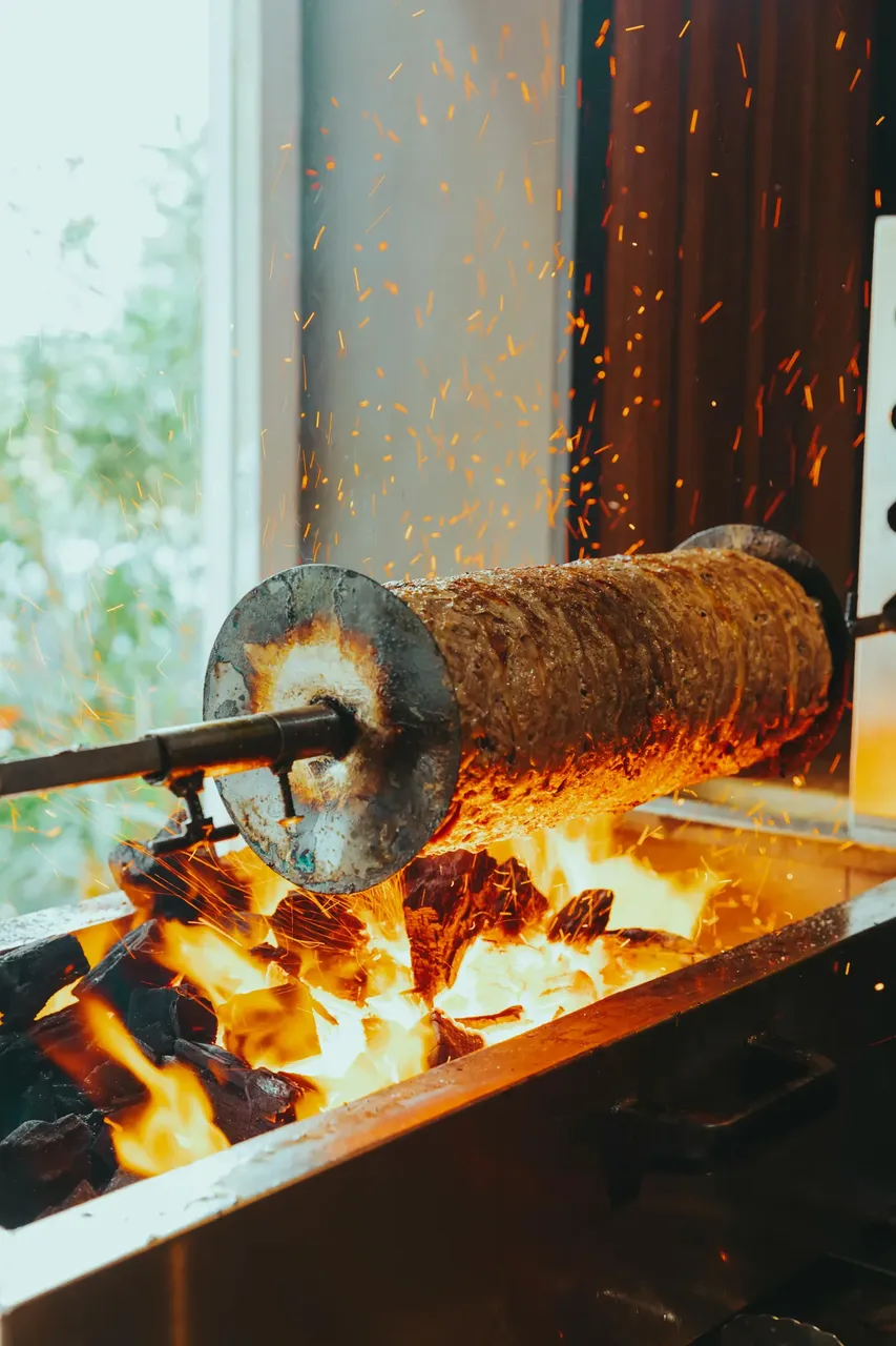 A large skewer of roasted meat slowly turning on a spit, ready to be sliced for making traditional Greek gyros, with a crispy, flavorful exterior