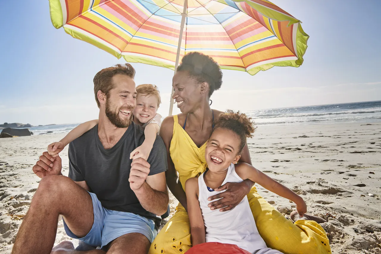 Family with two toddlers under the big umbrella at the beach, U.S.A.