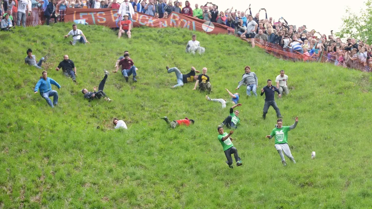 People jumping and rolling down a hill, chasing a roll of cheese — Shutterstock
