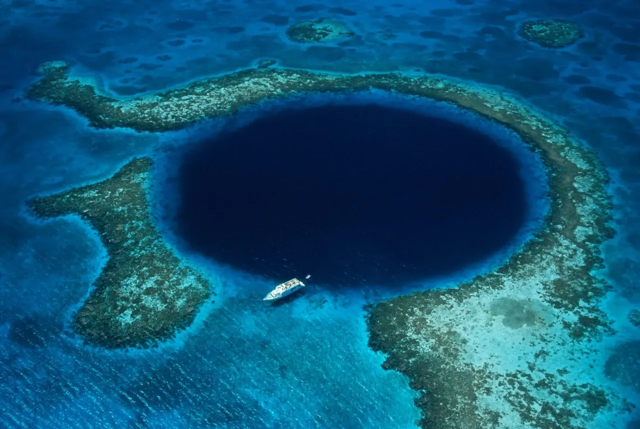 Vista aérea del Gran Agujero Azul de Belice, un gran pozo marino circular de azul intenso, rodeado de aguas turquesas.