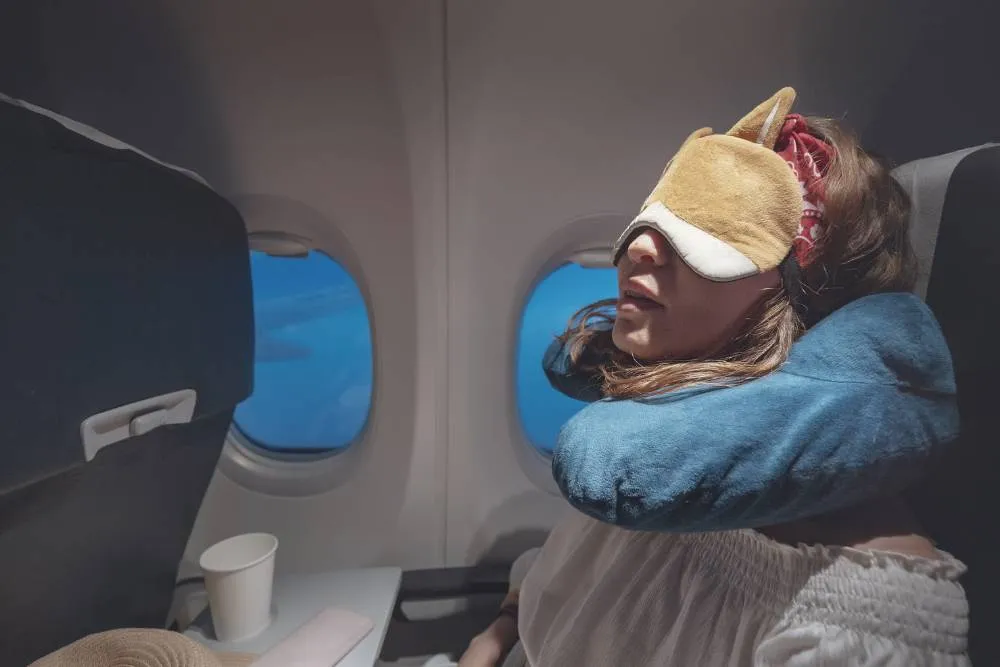 Person sleeping on airplane with eye mask and neck pillow — Getty Images