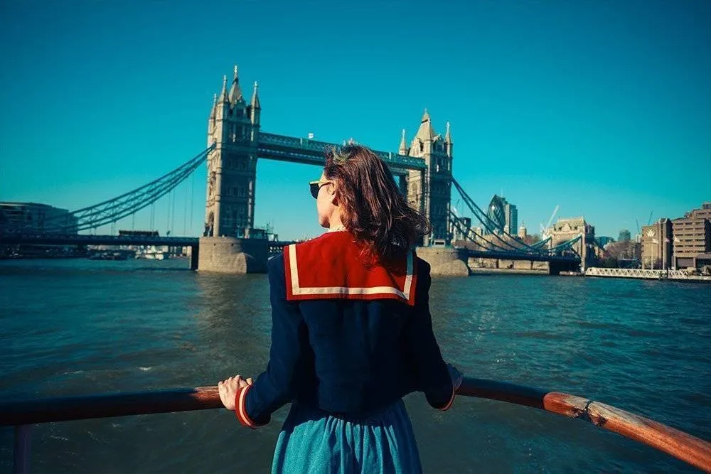 A young woman on a boat is looking at Tower bridge and the London skyline