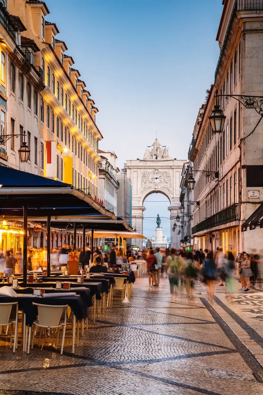 A street view of Baixa, Lisbon’s downtown area, leading toward the grand Arco da Rua Augusta, lined with shops and historic buildings.