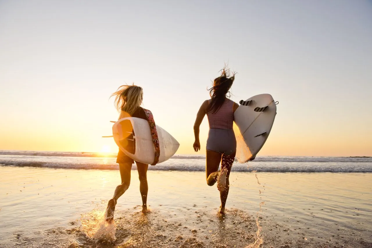 female surfers running on the beach at sunset, California, U.S.A.