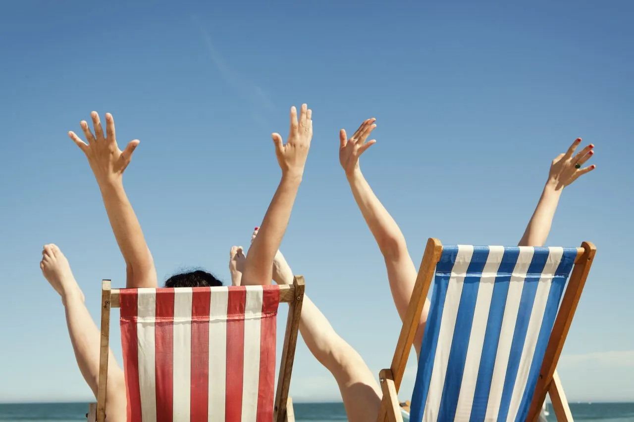 Women throwing arms and legs in air sitting in deckchairs, beach