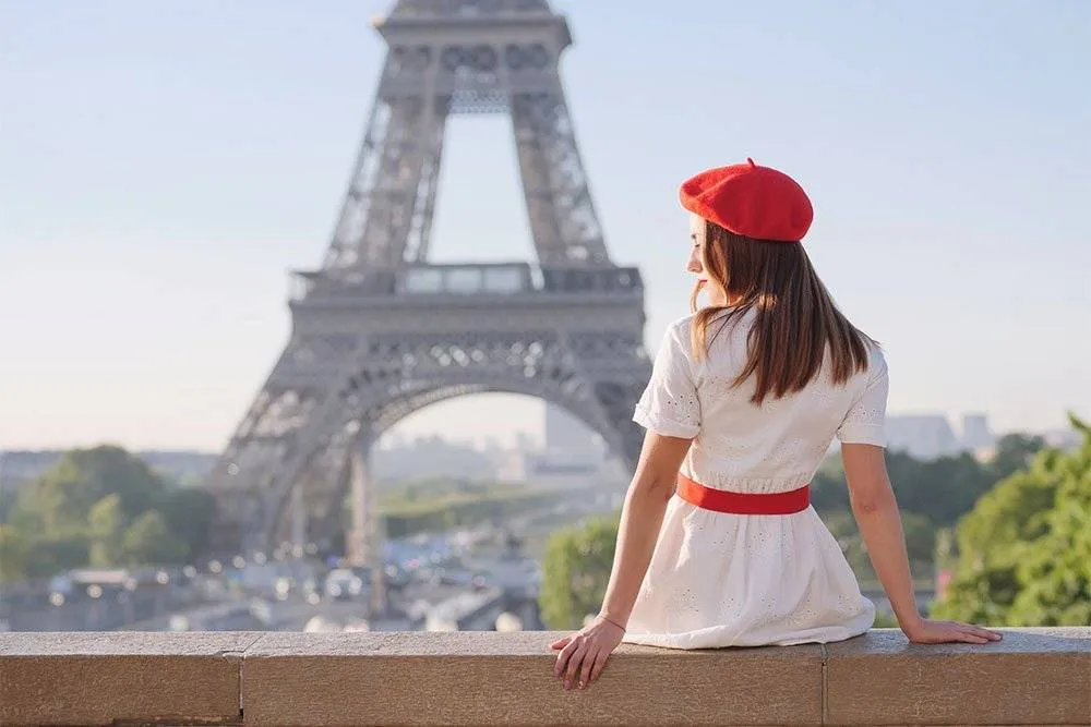 Girl in red beret sat on a wall with Eiffel Tower in the background — Shutterstock