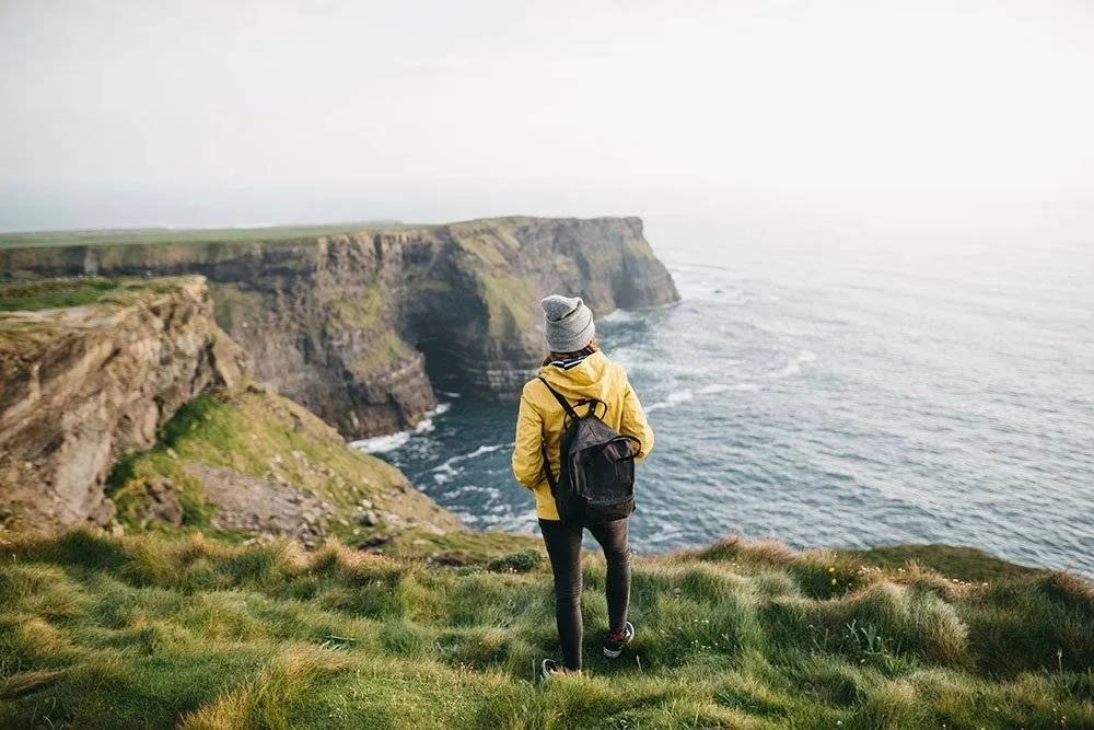 Fiatal hátizsákos turista áll a Cliffs of Moher-en sárga kabátban