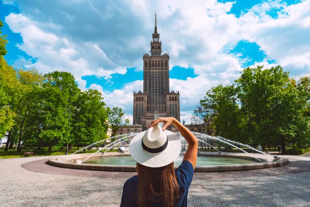 Woman in sun hat stood in front of Palace of Culture and Science in Warsaw — Getty Images
