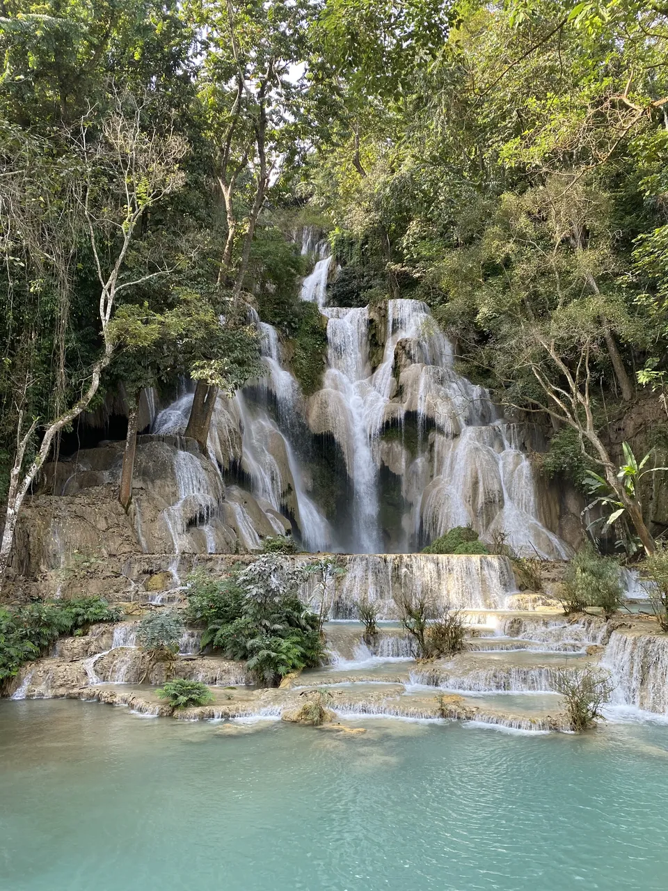 Majestic turquoise waters cascading down the multi-tiered Kuang Si Waterfall surrounded by lush greenery