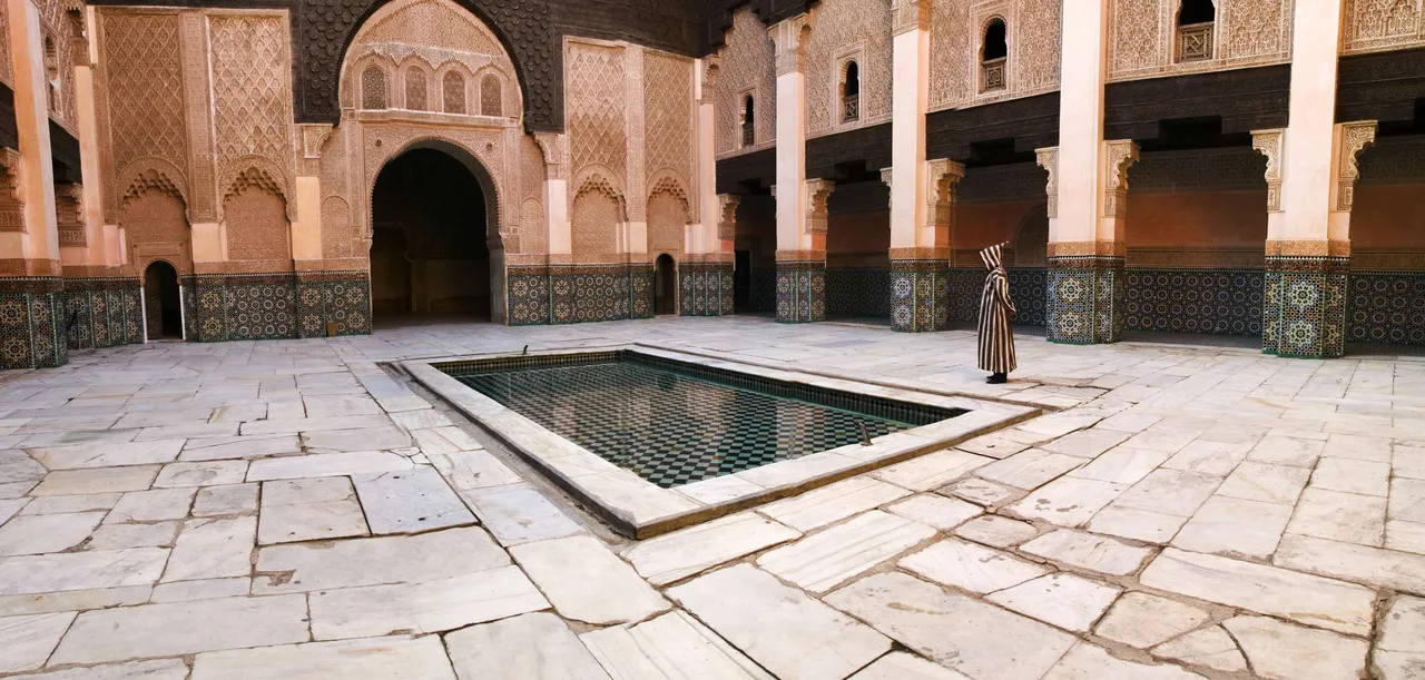 A man in a burnoose in the courtyard of the Ali ben Youssef Medersa in Marrakech, which dates from 1565.