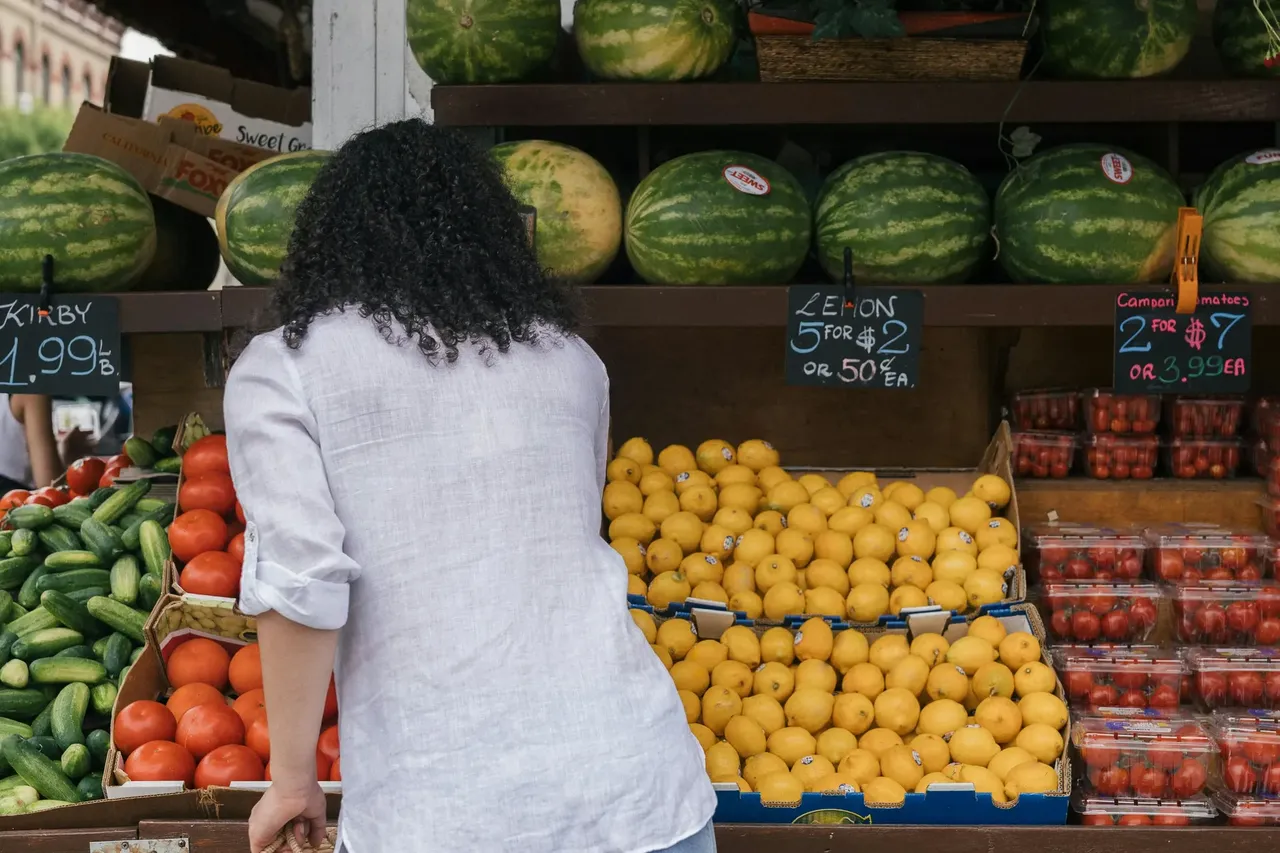 A bustling farmers market in Tilos, Greece, showcasing a variety of fresh local produce, fruits, vegetables, and traditional Greek goods, with vendors and shoppers interacting