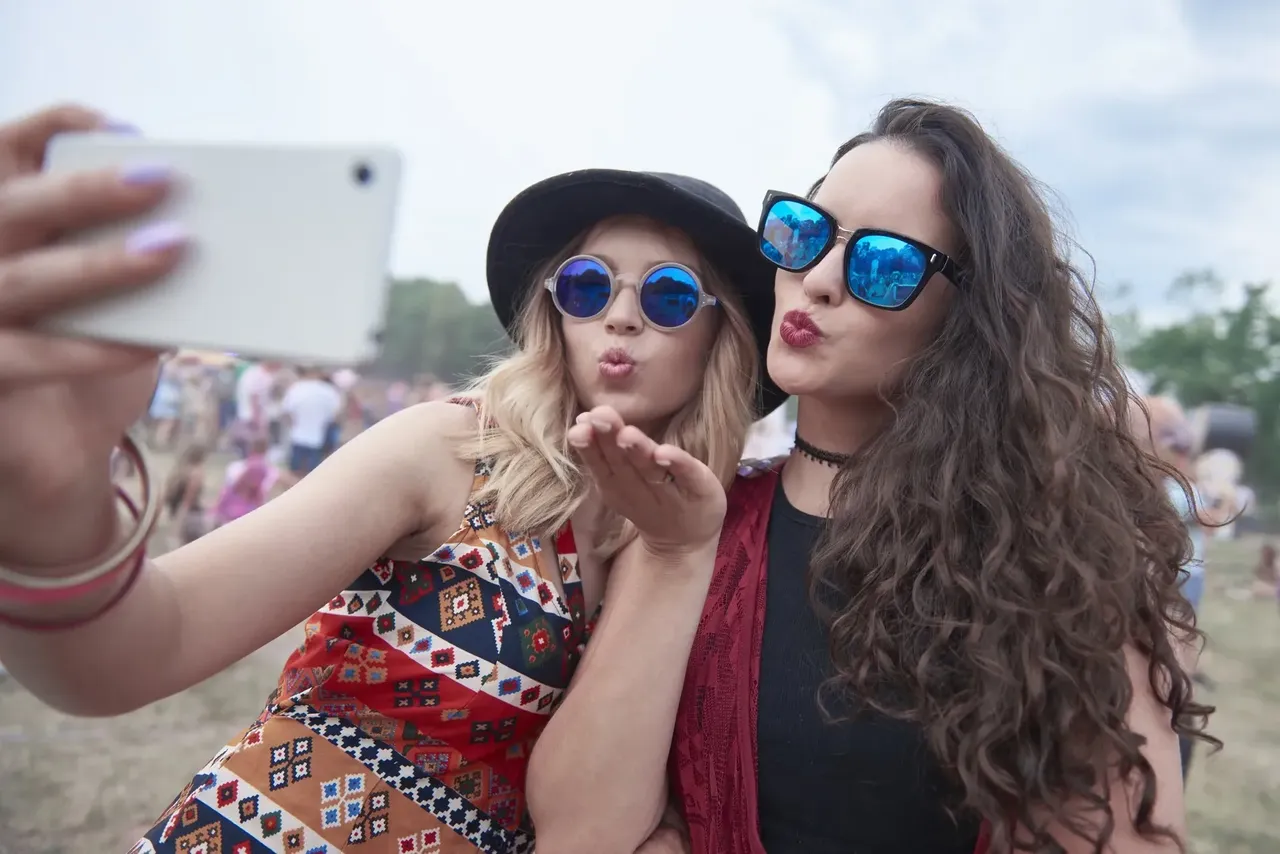 Dwie dziewczyny w okularach przeciwsłonecznych robią selfie na festiwalu.