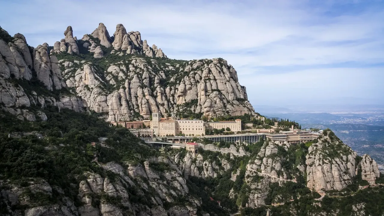 Stâncile abrupte din Montserrat, cu formațiuni stâncoase înalte care se ridică dramatic pe fundalul unui cer înnorat.