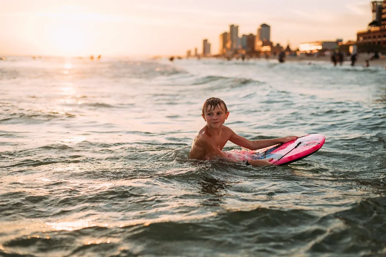 Young boy at sunset swimming in the ocean with cityscape background, Panama City Beach