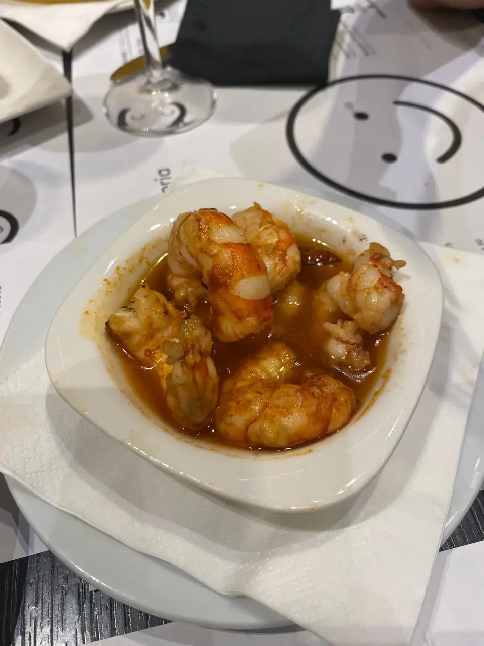 Un mic preparat din creveți și usturoi la restaurantul Güell Tapes, servit pe o masă din lemn cu o atmosferă rustică.