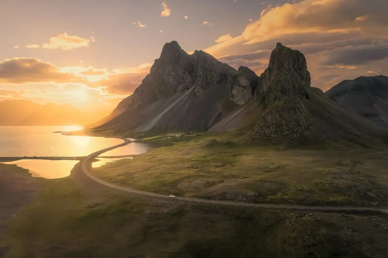 A Vestrahorn látványos csúcsai Stokksnesnél a naplemente aranyló fényében egy, a tengerhez vezető, kanyargós partmenti úttal