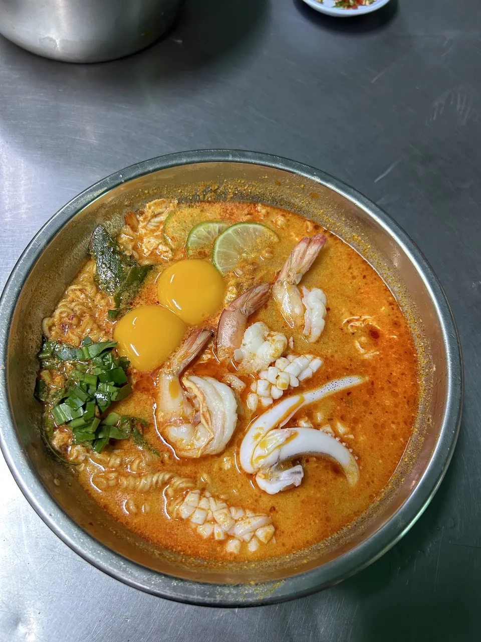 Kouřící miska polévky Tom Yum s krevetami, houbami, citronovou trávou, lístky kafírové limetky a chilli, ozdobená čerstvým koriandrem a plátky limetky