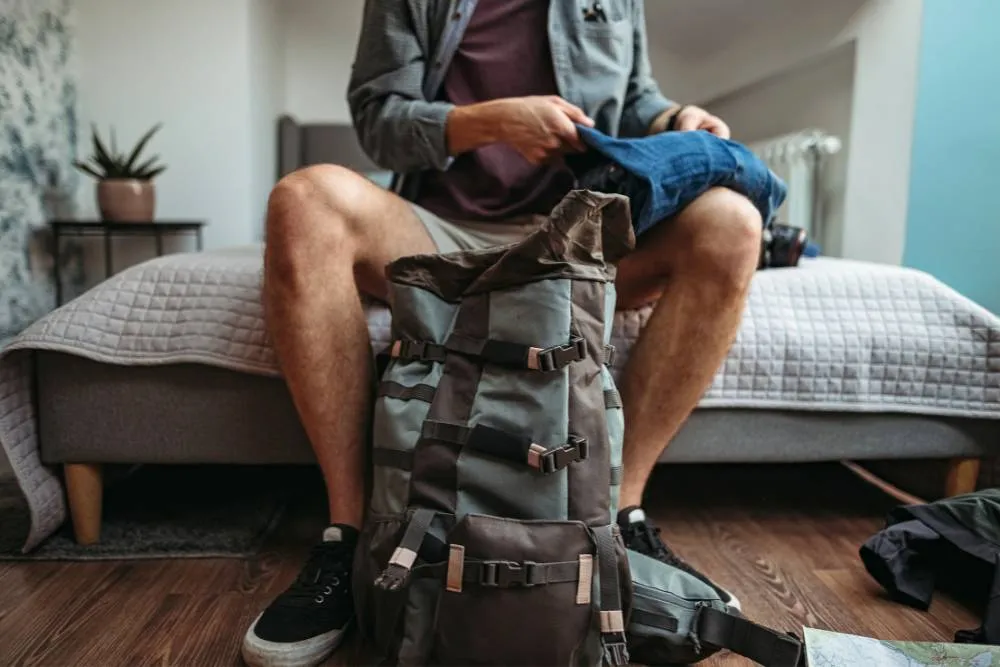 Person sat on bed packing backpack — Getty Images