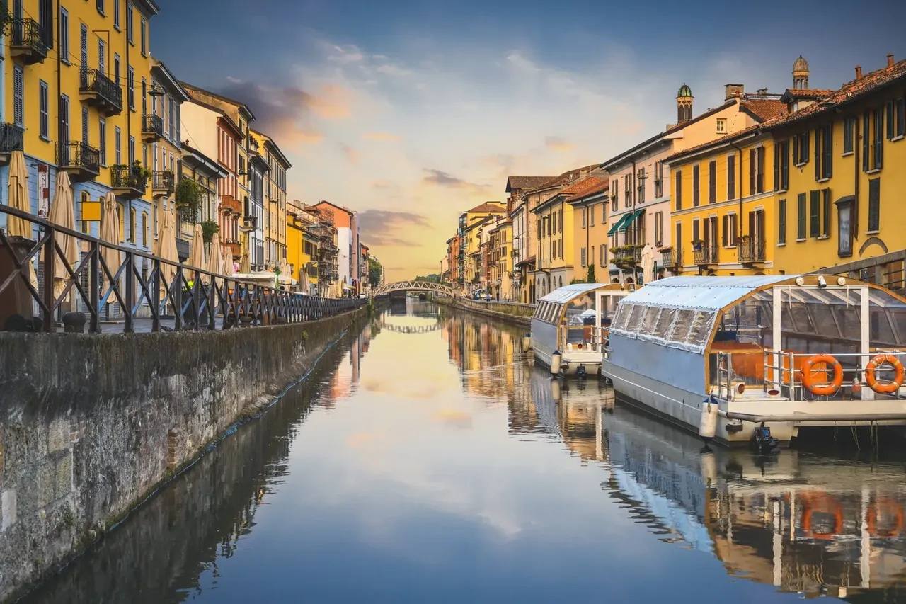 Canalele liniștite din Navigli, Milano ,la apus, cu strălucirea caldă a soarelui la apus reflectându-se în apă și clădirile pitorești care mărginesc canalele.