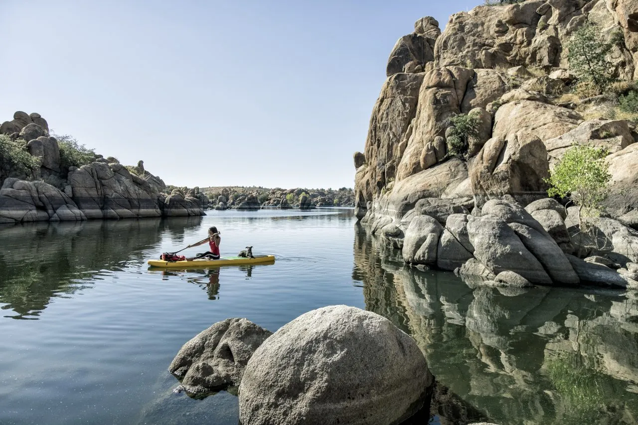 Woman sitting on paddle board on lake with puppy, Arizona, USA
