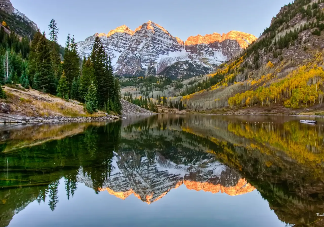 Snow-capped Rocky Mountains surrounding the resort town of Aspen, Colorado, with dense forests and ski slopes in the background.