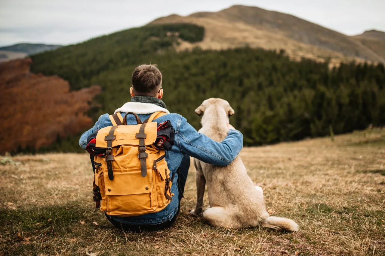 Hiker with backpack and his dog resting on mountain