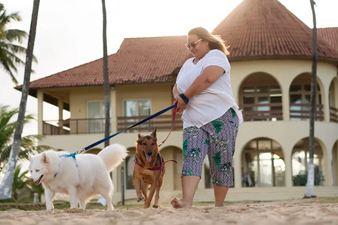 woman walking siberian husky and german shepherd next to a beach house