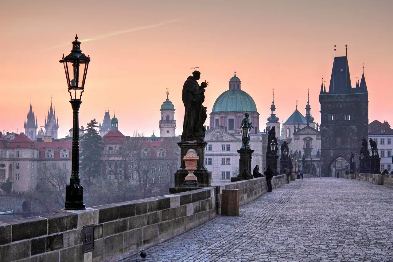 Charles Bridge at dawn with its statues and lampposts silhouetted against a soft pink sky