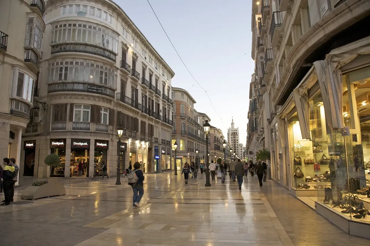 Upscale shops and shoppers at dusk on pedestrian street Calle de Larios, Malaga, Costa del Sol, Andalucia, Spain