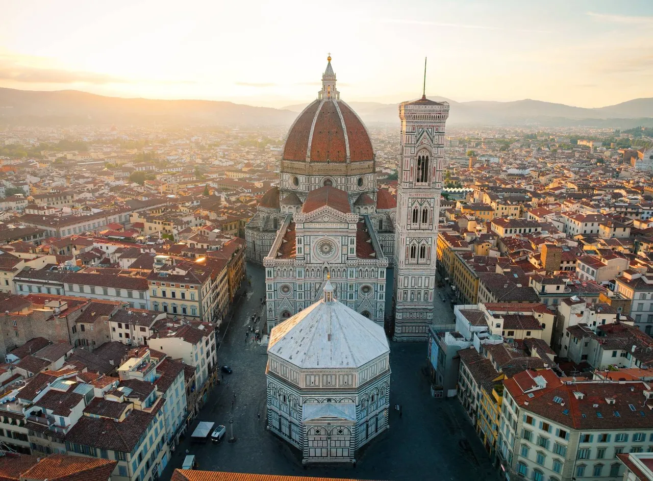 Úchvatný letecký pohled na florentský Dóm (Duomo di Firenze) za svítání, s ikonickou červenou kopulí a okolní historickou zástavbou zalitou zlatým světlem