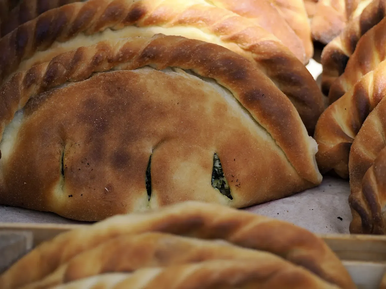 Un prim-plan cu panzerotti proaspăt prăjiți, aurii și crocanți la exterior, cu o umplutură delicioasă de brânză și roșii la interior.