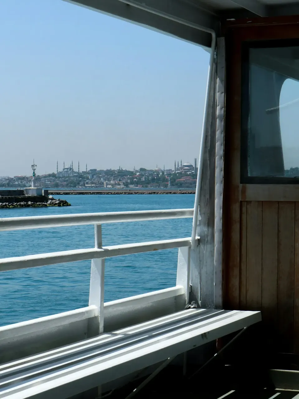 A scenic view from a Bosphorus cruise, showing the sparkling waters of the Bosphorus Strait with historic buildings and modern cityscape on both sides, and a bridge in the distance.
