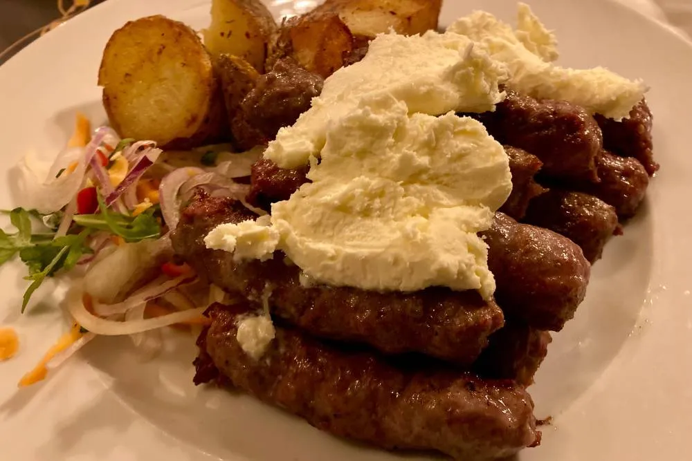 Ćevapi and kaymak on plate with potatoes and salad — Getty Images