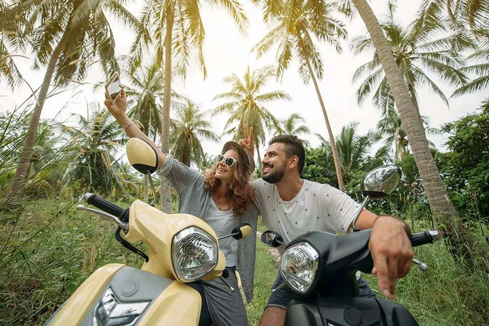 A loving couple travels by scooter through the jungle in Southeast Asia. We stopped among the palm trees. Smiling happily and taking selfies