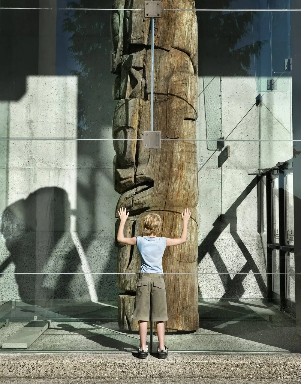 Un niño de pie frente a un alto tótem de madera tallada a mano en el Museo de Antropología de Vancouver.