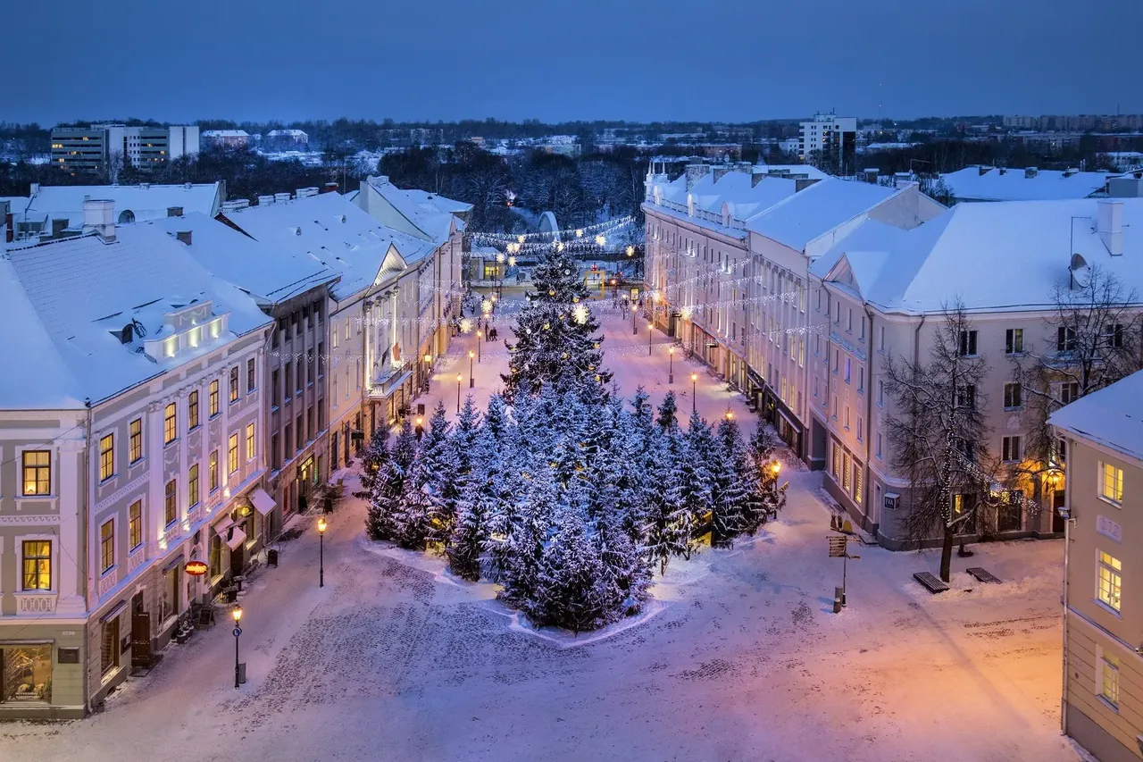 Snow-covered Tartu, Estonia, viewed from above at night, with glowing holiday lights highlighting the town square