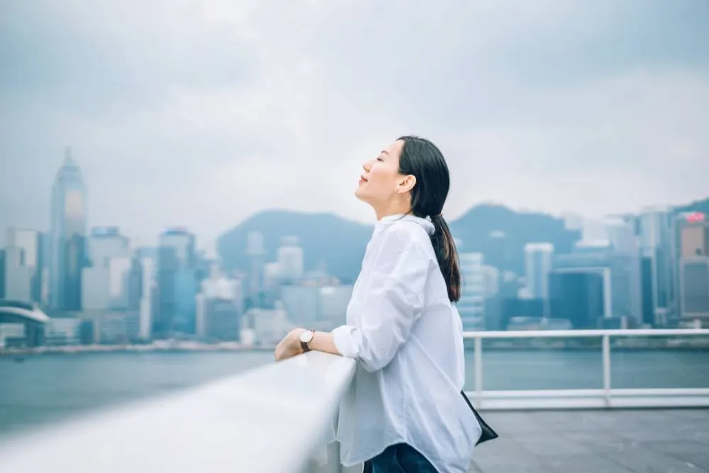 Woman with closed eyes doing breathwork against city backdrop — Getty Images