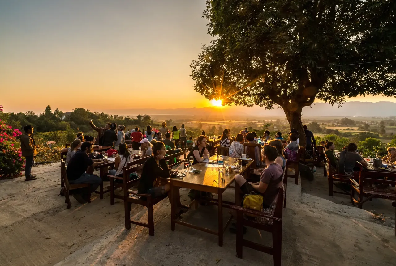 Sunset over a valley in Myanmar with people dining in foreground — Shutterstock