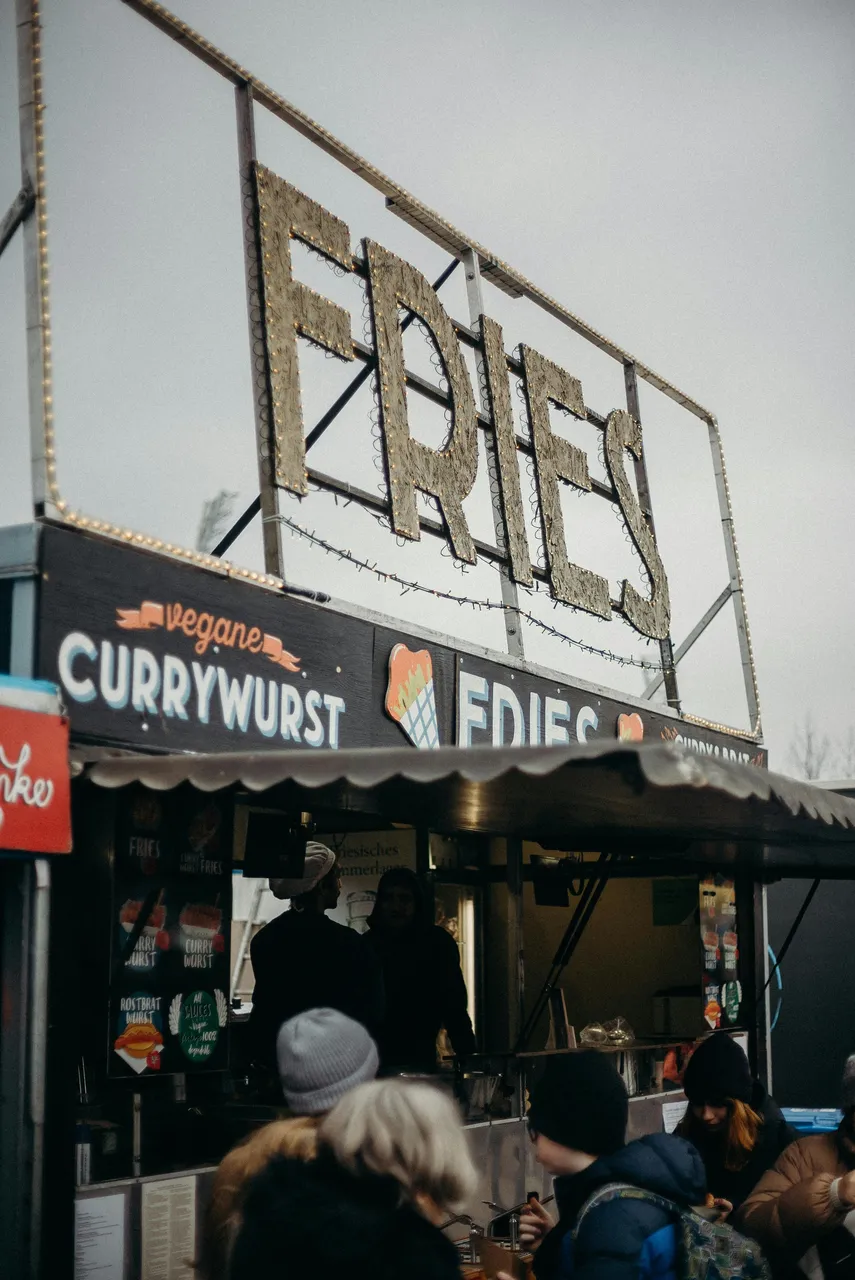 Food truck in Cologne serving currywurst fries, with a lot of signage and customers enjoying street food outdoors