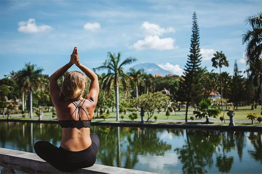 Woman practicing a yoga pose in front of a pool with rural Balinese scenery in the background — Shutterstock