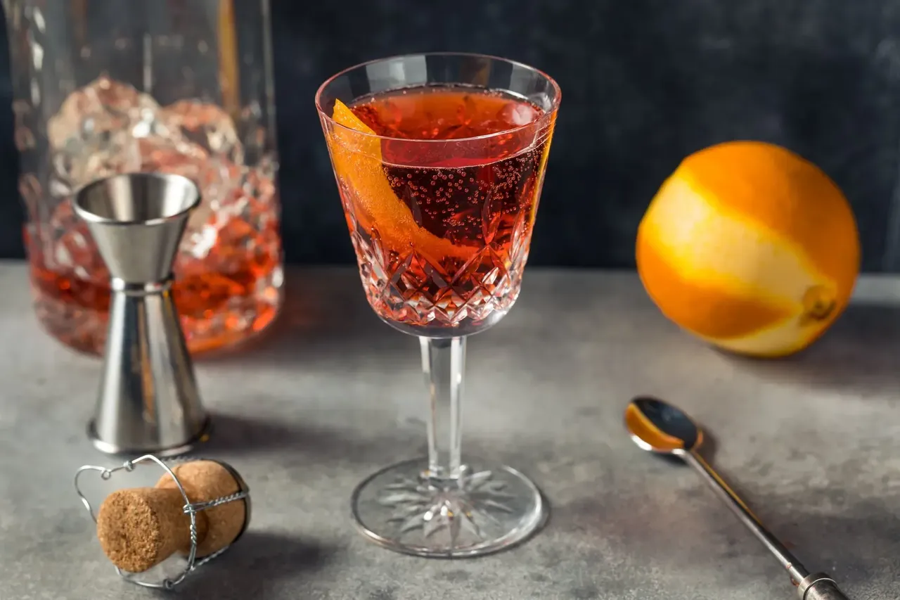 Un prim-plan al unui cocktail Negroni Sbagliato, cu un amestec de vin spumant, Campari și vermut, garnisit cu o felie de portocală.