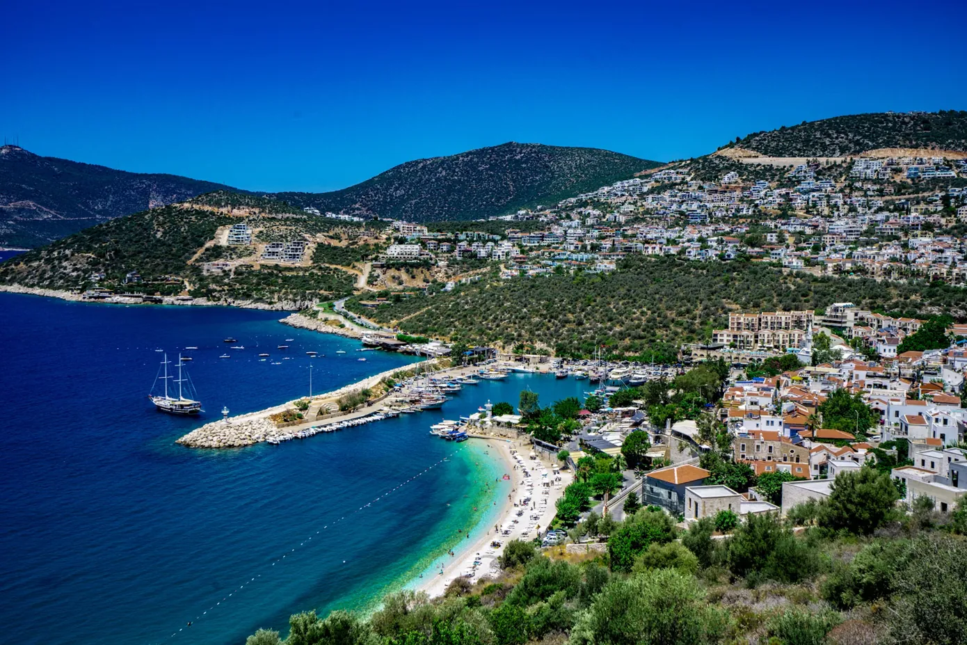 White buildings on a green hillside above a harbor beach on Turkey’s Turquoise Coast near Antalya