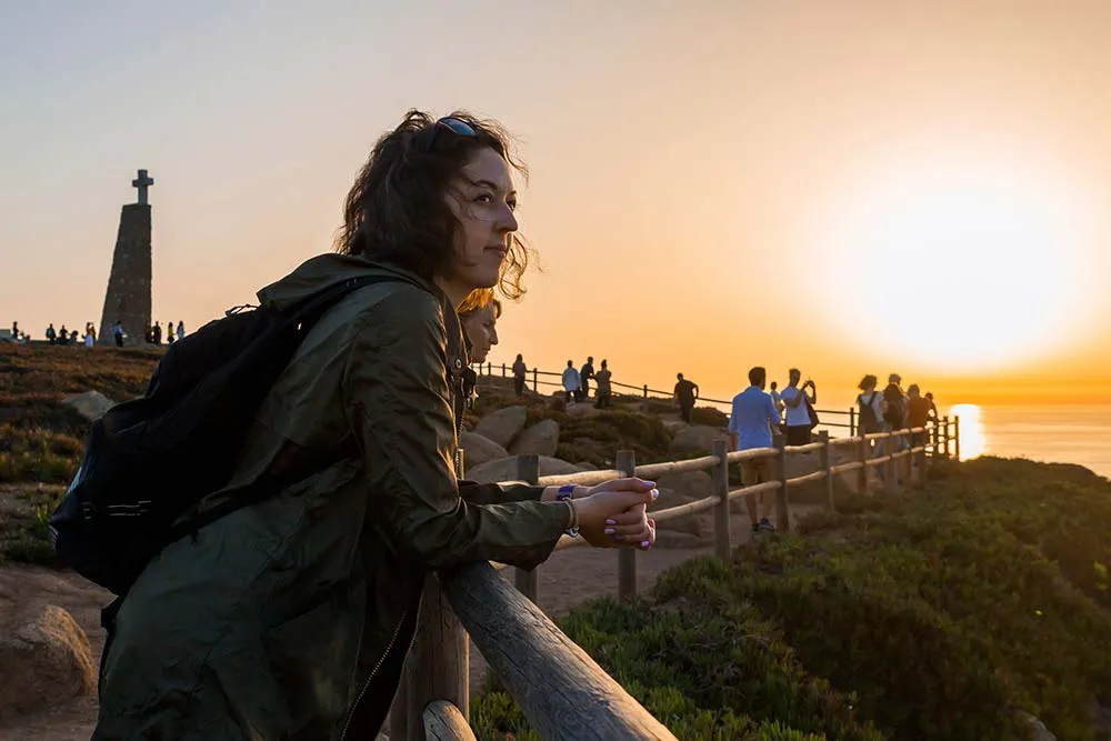 Portrait of young and caucasian woman enjoying amazing sunset on Cabo da Roca, Portugal. She is looking somewhere far away.