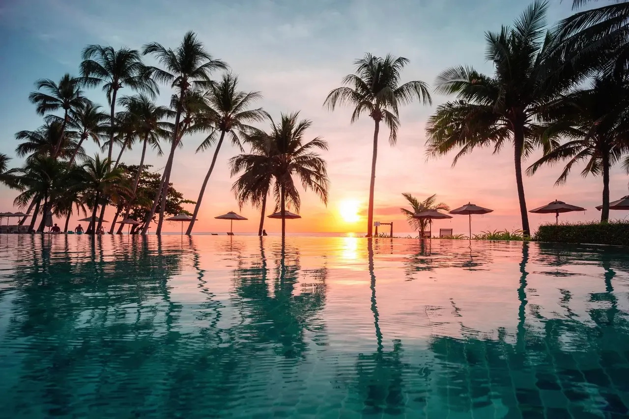 Beautiful tropical beach front hotel resort with swimming pool and palm trees during a warm sunny day