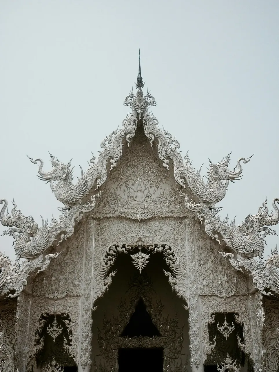 The stunning white facade of Wat Rong Khun (White Temple), with its intricate details, reflective surfaces, and ethereal, almost otherworldly appearance.