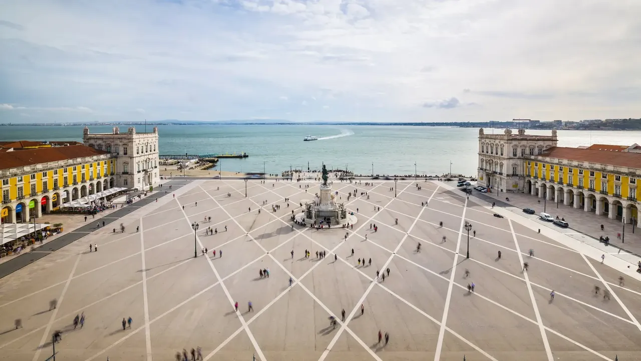 A wide view of Praça do Comércio, Lisbon’s famous waterfront square, showcasing its yellow buildings and grand statue of King José I in the center.
