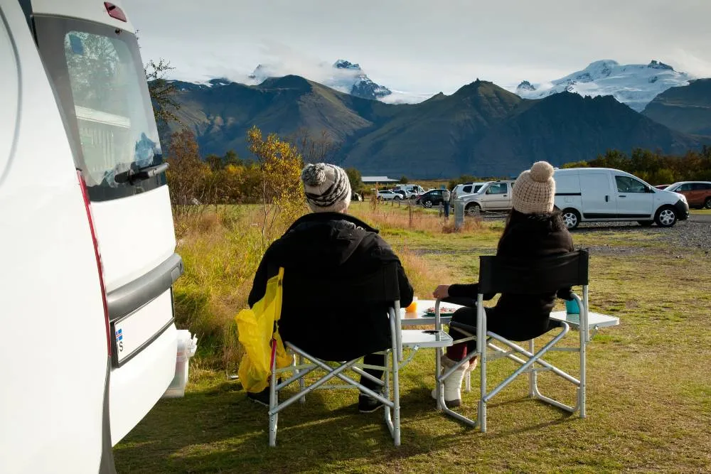 Couple sitting on camping chairs on campsite in Iceland — Getty Images