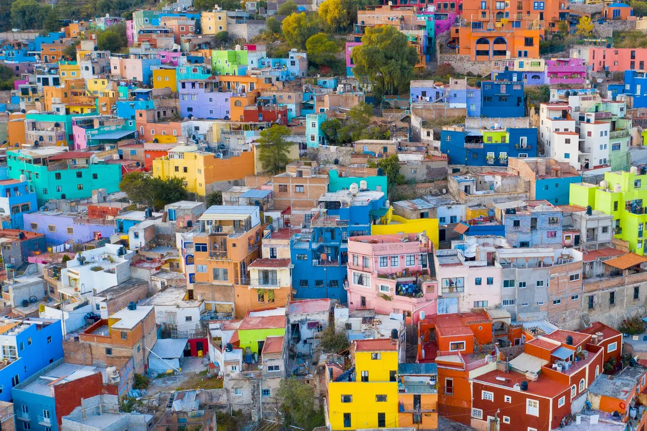 A mexikói Guanajuato vibráló jelenete, tele élénk színű házakkal, amelyek a domboldalon lezuhanva élénk vörös, sárga, kék és zöld színű foltokat alkotnak.